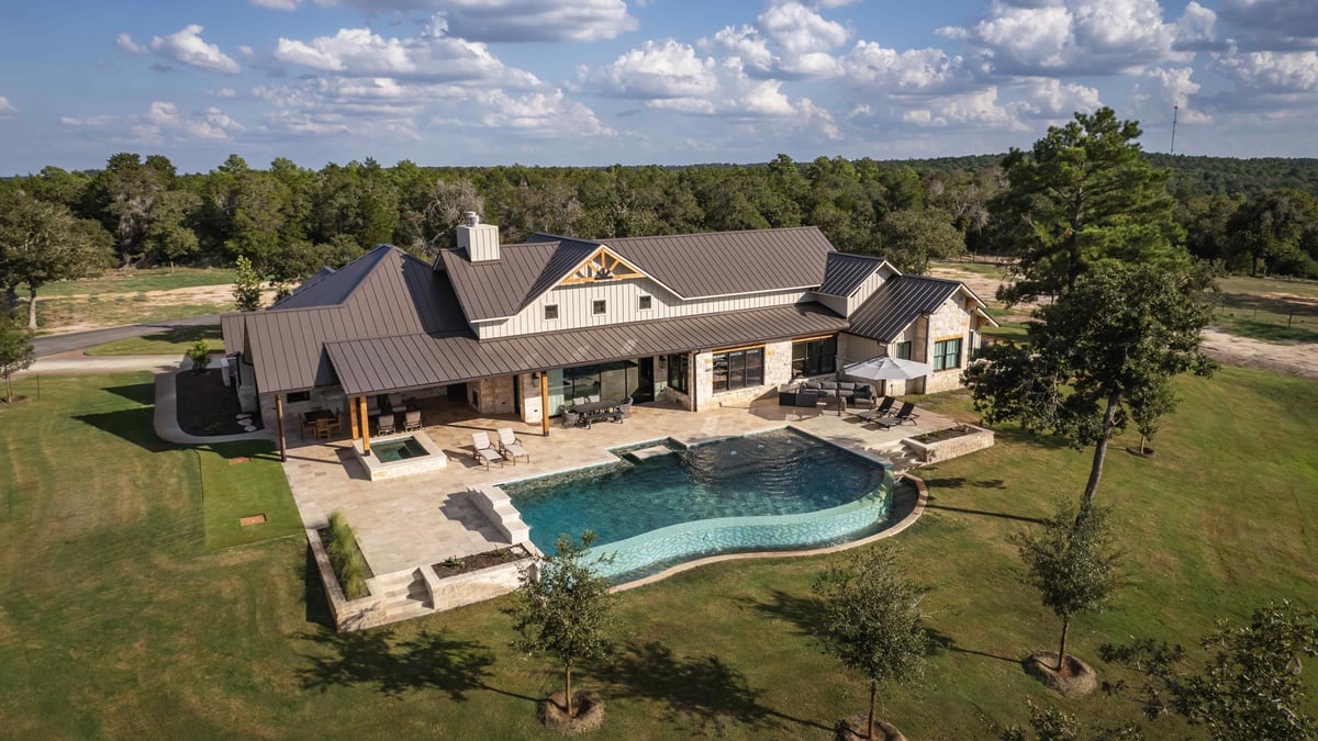 Backyard view of a house with a pool, large patio, and metal roof in central Texas | J Bryant Boyd