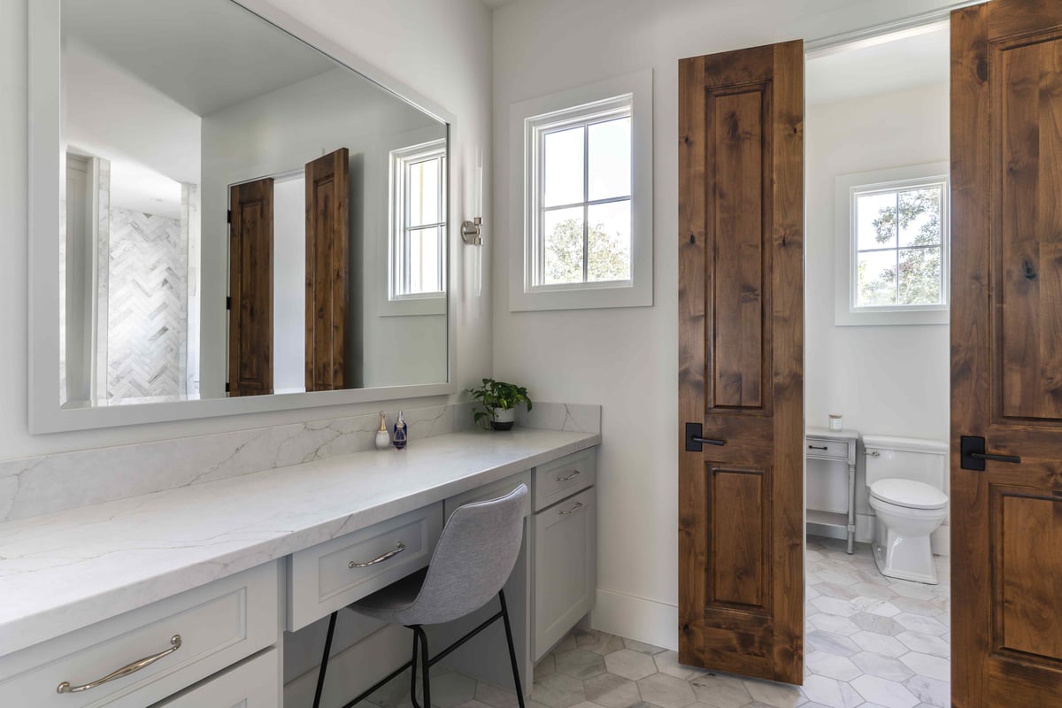 Bathroom vanity area with a large mirror, a chair, and natural light from windows | J Bryant Boyd