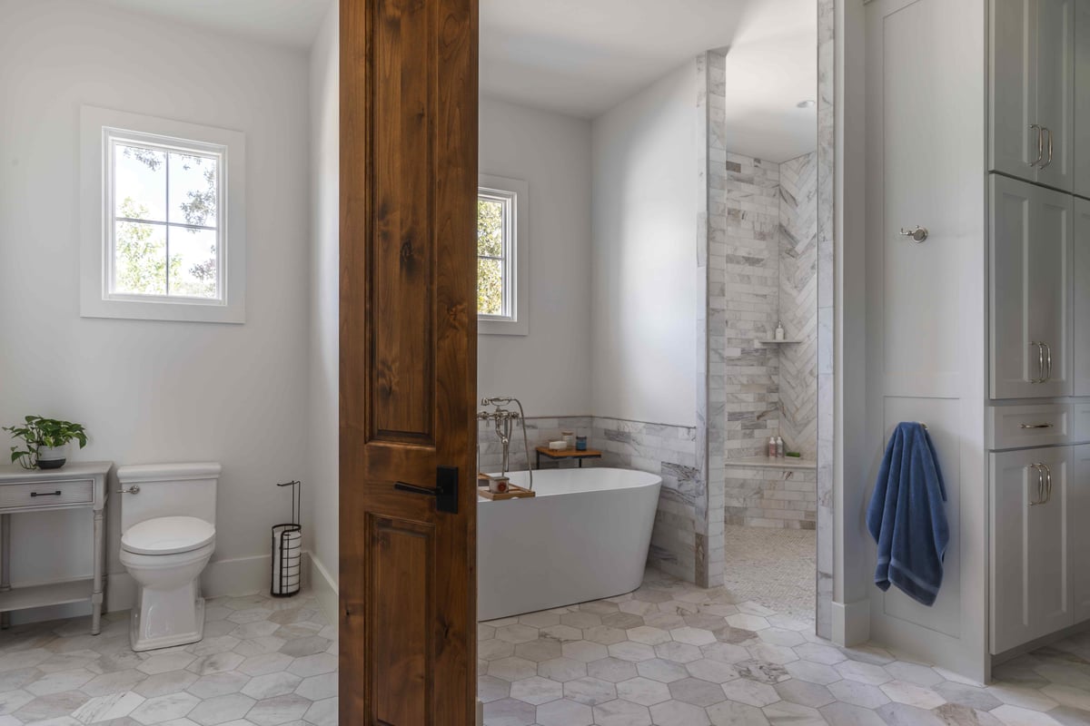 Bathroom with a freestanding tub, hexagonal floor tiles, and a wooden door | J Bryant Boyd