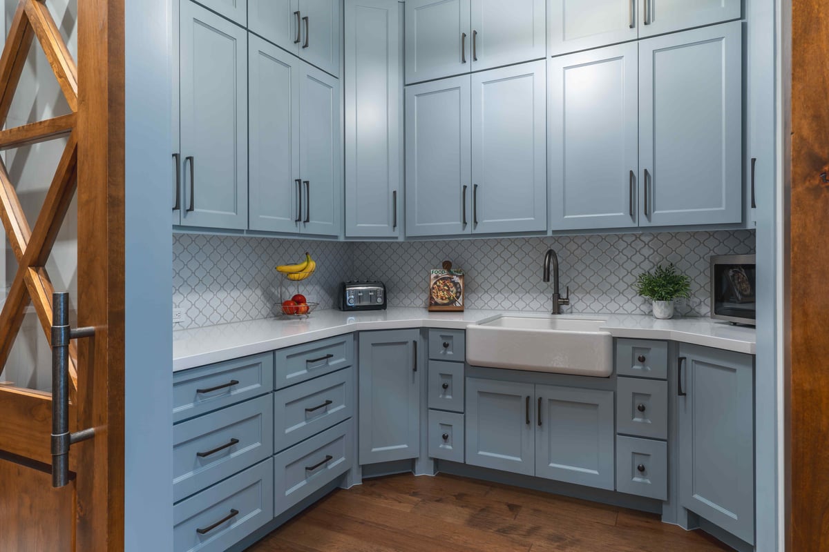 Compact kitchen with blue cabinetry, white countertops, and a farmhouse sink | J Bryant Boyd