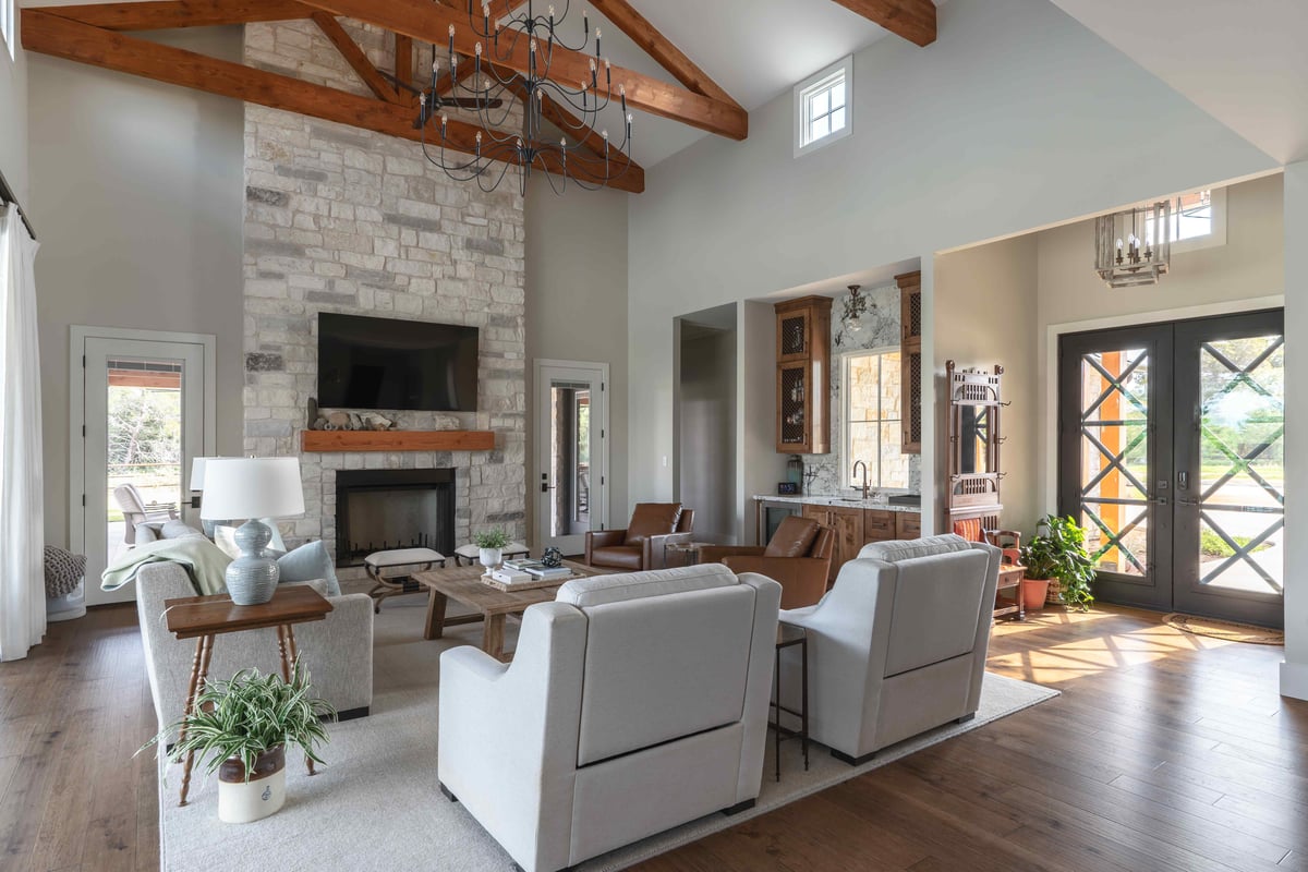 Living room featuring a stone fireplace, exposed beams, and an entryway with double doors in central Texas | J Bryant Boyd