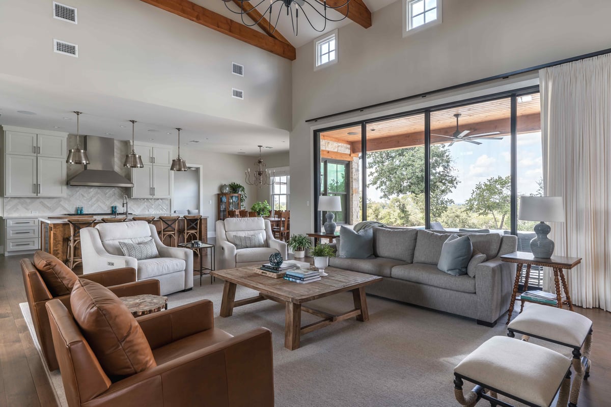 Living room with a mix of seating options, large windows, and a view into the kitchen in central Texas | J Bryant Boyd