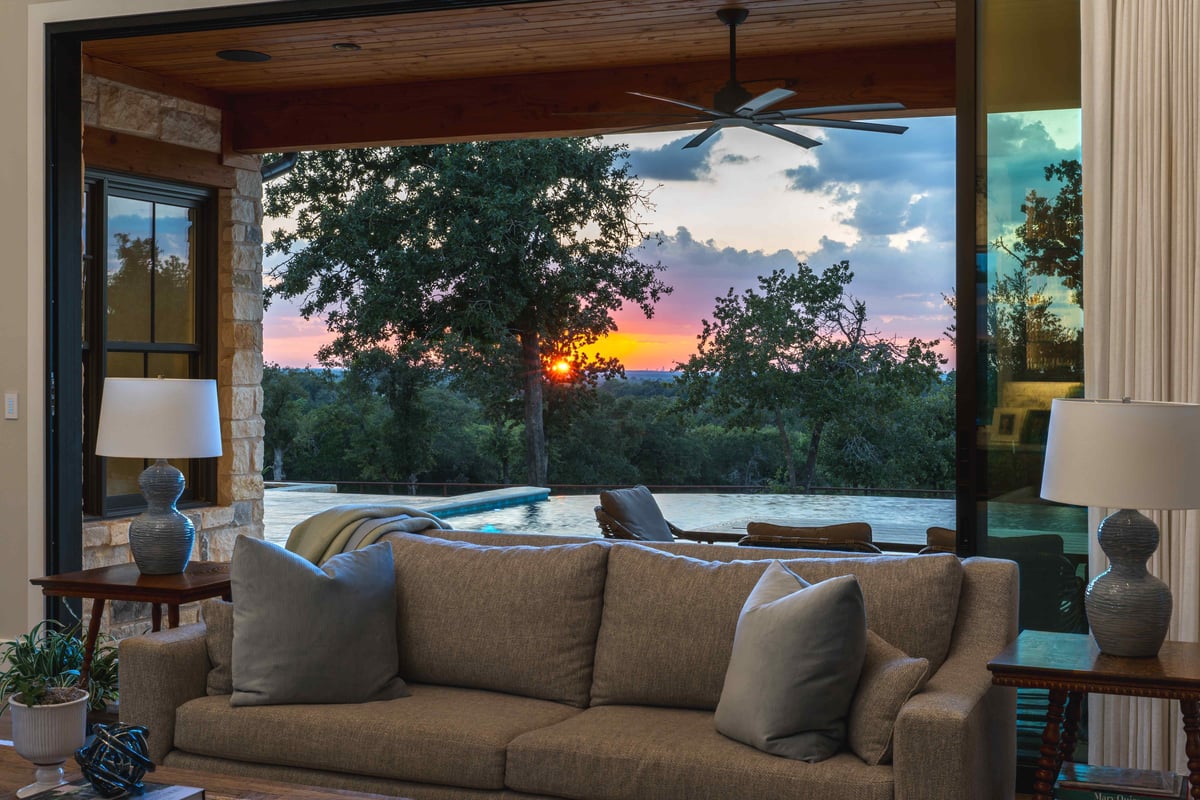 Living room with a sofa facing an open view of a sunset over a pool and trees in central Texas | J Bryant Boyd