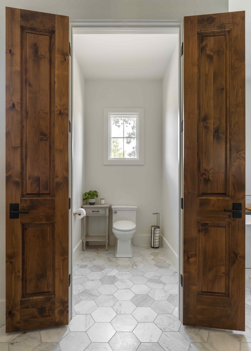 Small toilet room with a wooden door, window, and minimal decor | J Bryant Boyd