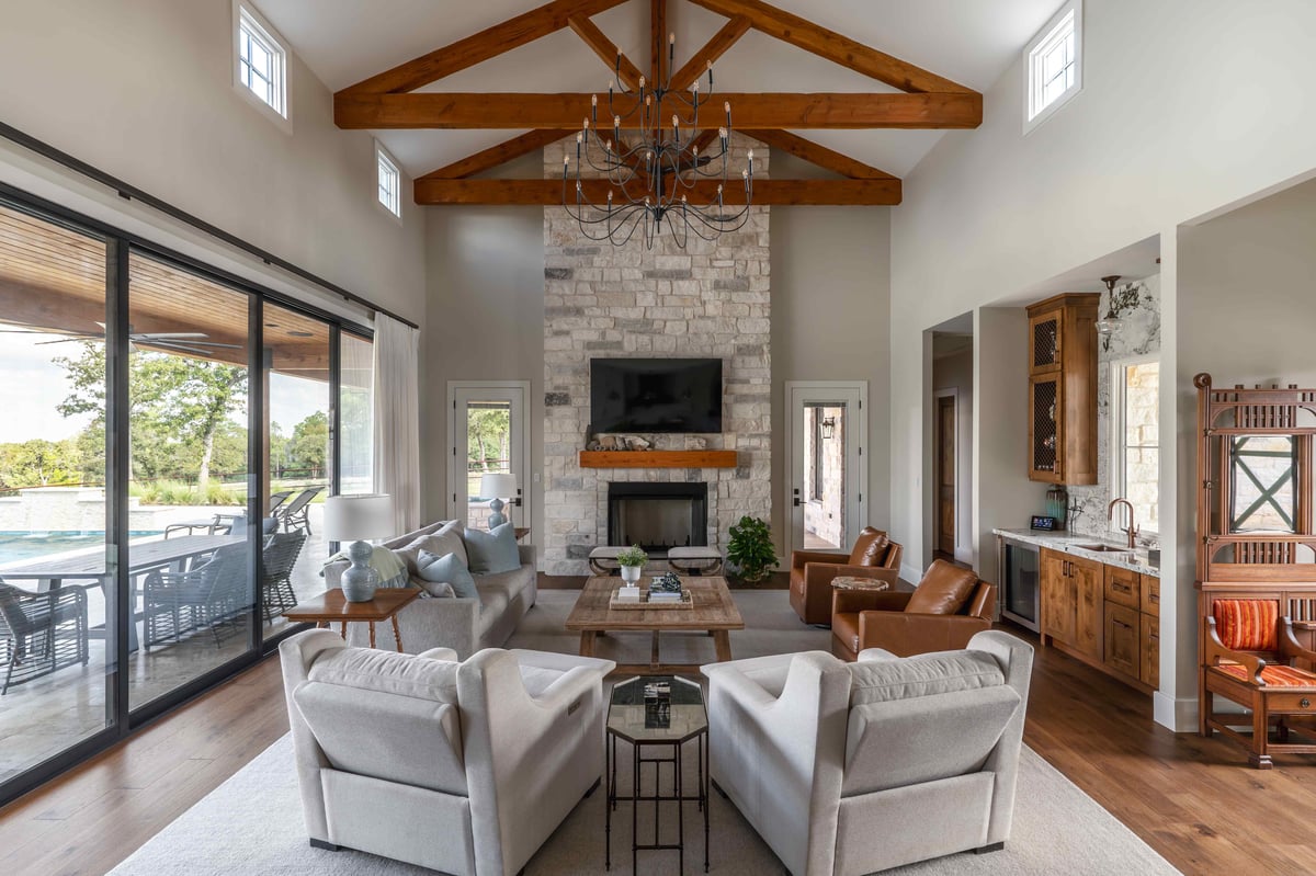 Spacious living room with exposed wooden beams, a stone fireplace, and large windows in central Texas |J Bryant Boyd