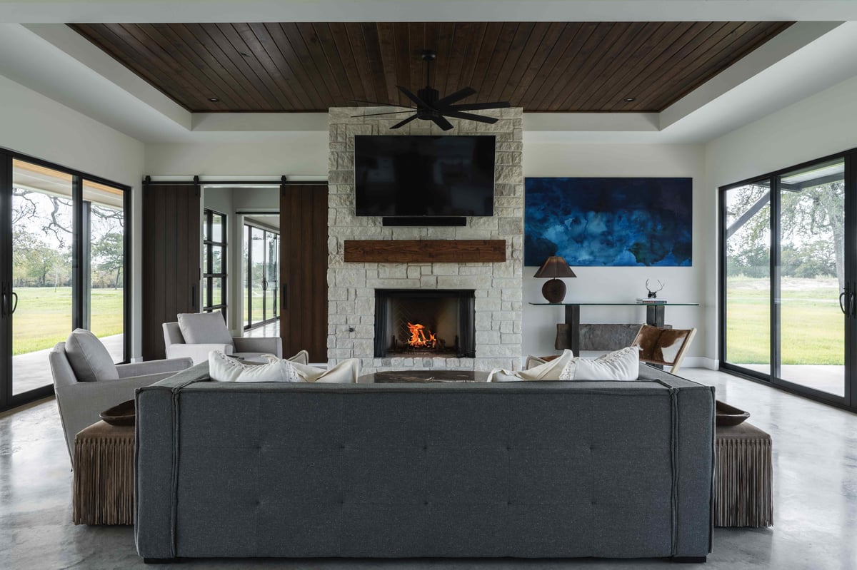 A living room with a stone fireplace, a large TV mounted above it, and comfortable seating | J Bryant Boyd