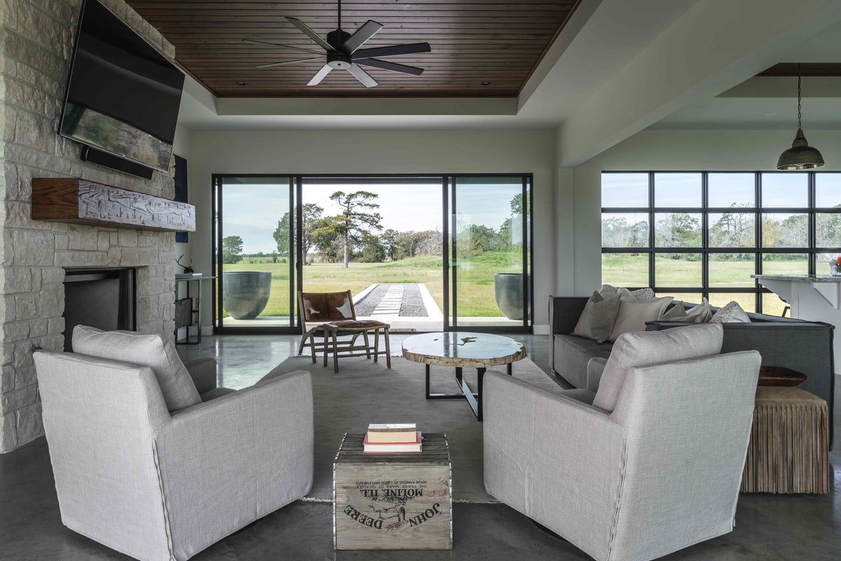 A living room with a stone fireplace, a large TV, and modern seating. The room has large sliding doors opening to the outdoor area | J Bryant Boyd