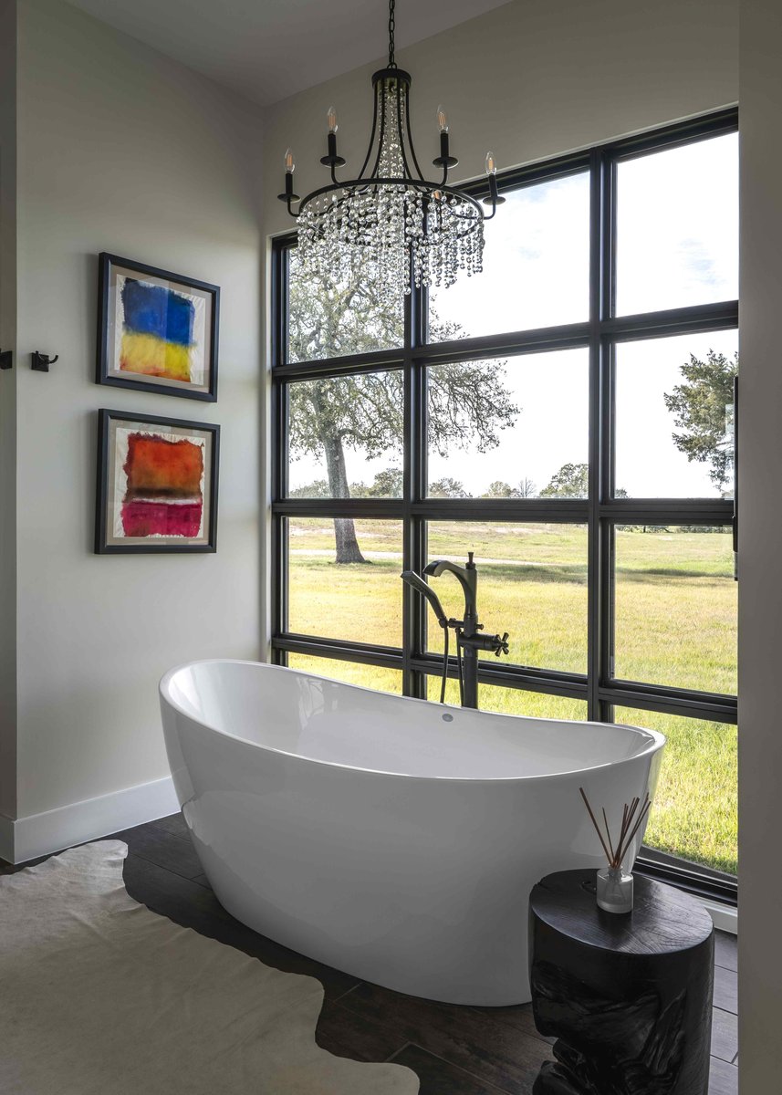 Bathroom featuring a freestanding tub by large windows, a chandelier, and colorful abstract paintings on the wall | J Bryant Boyd