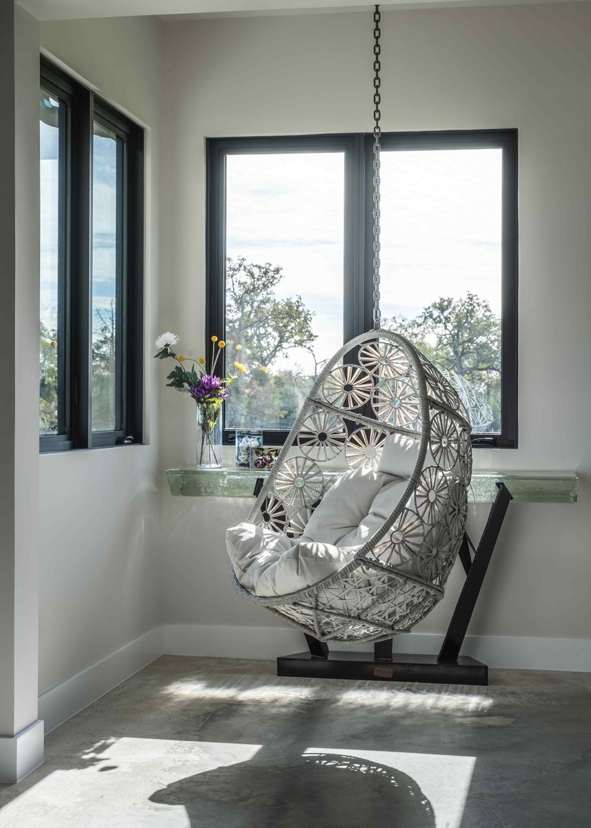 Close-up of a white hanging chair with floral patterns in a sunlit nook, complemented by a vase of flowers | J Bryant Boyd