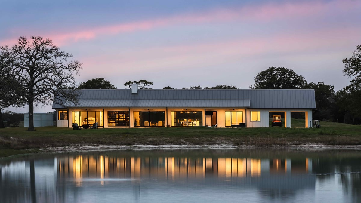 Evening view of a modern farmhouse with large windows and a reflecting pond. | J Bryant Boyd