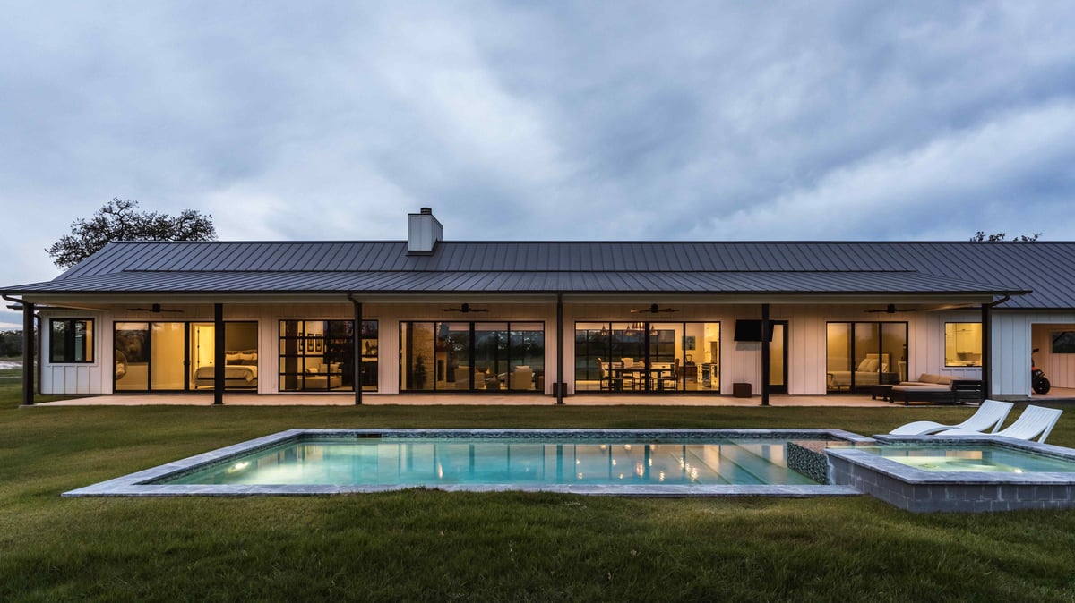 Modern farmhouse with a pool and large windows, viewed in the evening. | J Bryant Boyd