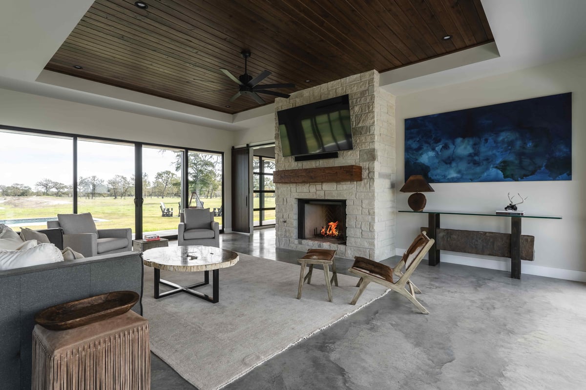 Modern living room with a stone fireplace, large windows, and neutral furniture. | J Bryant Boyd