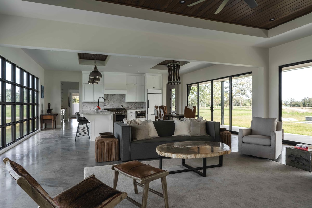 Open-plan living area with a view of the outdoors, featuring a stone fireplace and large windows. | J Bryant Boyd