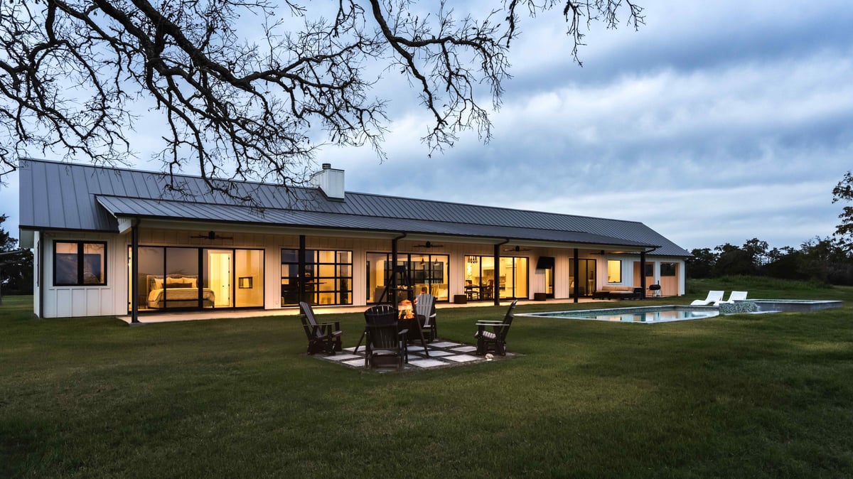 Outdoor view of a modern farmhouse with a fire pit and swimming pool. | J Bryant Boyd