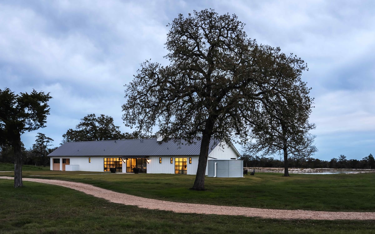 Rural modern farmhouse with a tree-lined driveway and a view of the pond | J Bryant Boyd