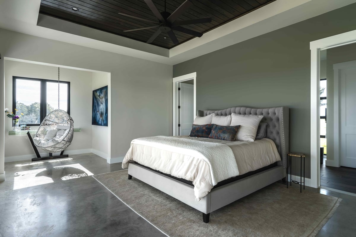 Spacious bedroom with gray walls, a tufted bed, and a white hanging chair in a sunlit nook | J Bryant Boyd