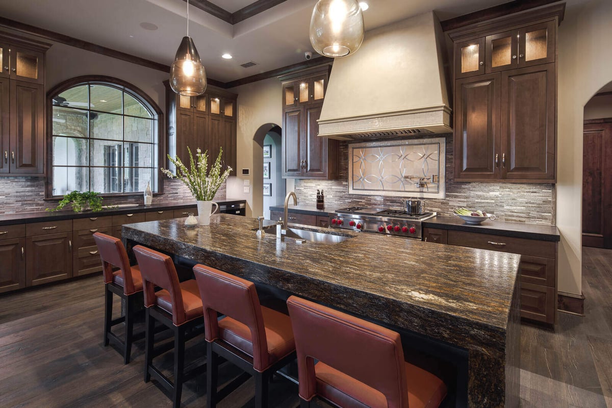 Custom kitchen with a large granite island and pendant lighting in a J Bryant Boyd home, Georgetown, TX