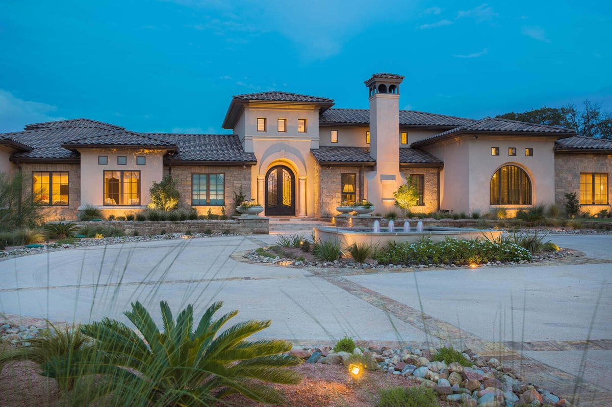 Custom luxury home with stone detailing and a central fountain at dusk by J Bryant Boyd in Georgetown, TX