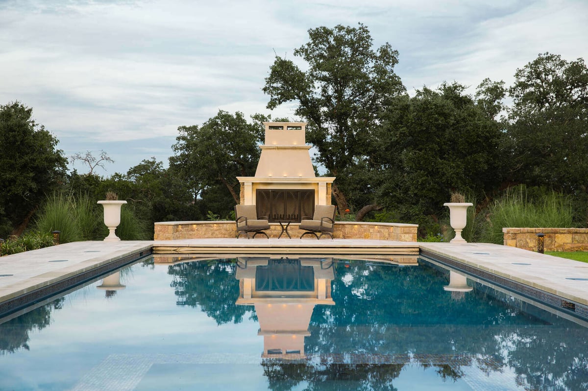 Custom outdoor fireplace and pool area with surrounding greenery in Georgetown, TX by J Bryant Boyd