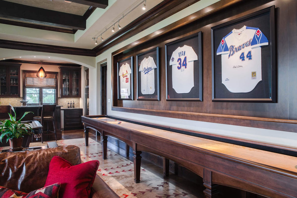 Luxurious custom home game room with framed sports jerseys and shuffleboard table by J Bryant Boyd in Georgetown, TX