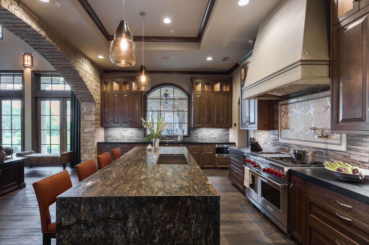 Luxury kitchen with expansive granite island and dark wood cabinets by J Bryant Boyd in Georgetown, TX