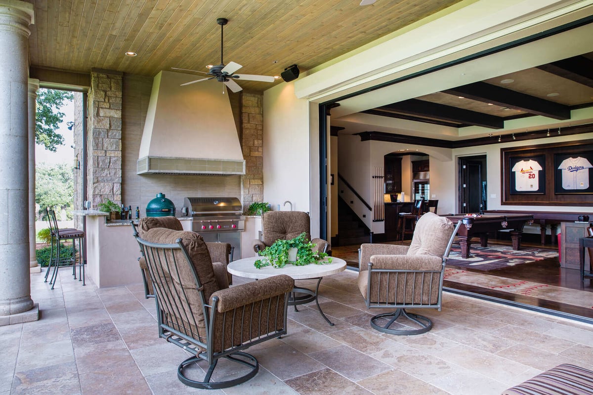 Outdoor patio with seating area and built-in grill opening into game room by J Bryant Boyd in Georgetown, TX