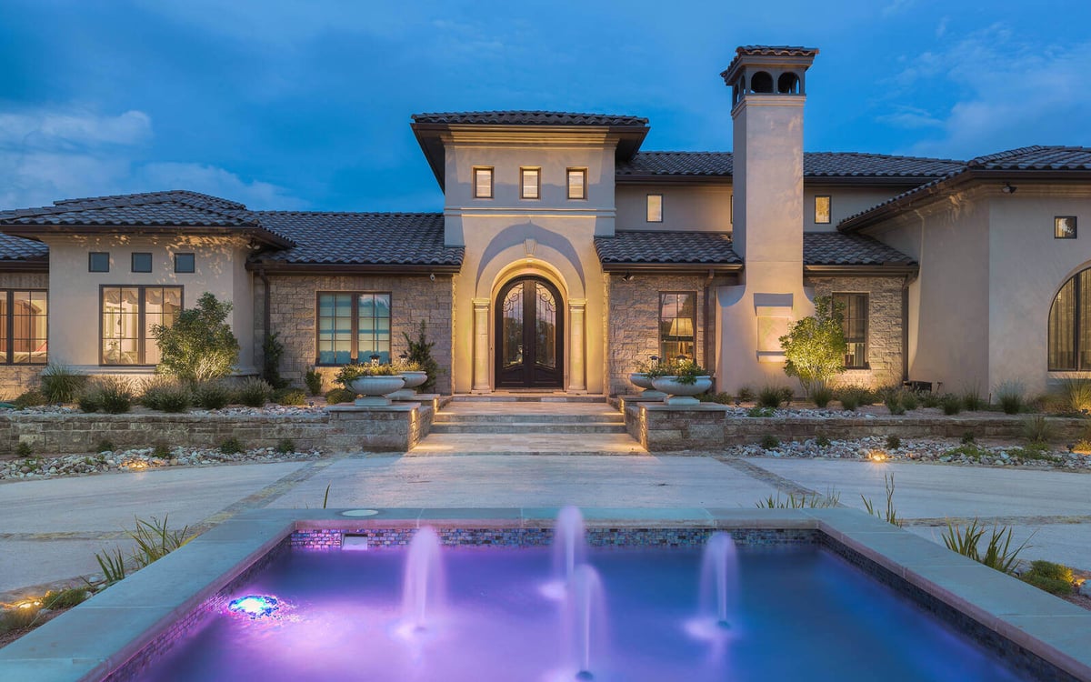 Stunning night view of a custom-built home with stone facade and a lit fountain by J Bryant Boyd in Georgetown, TX