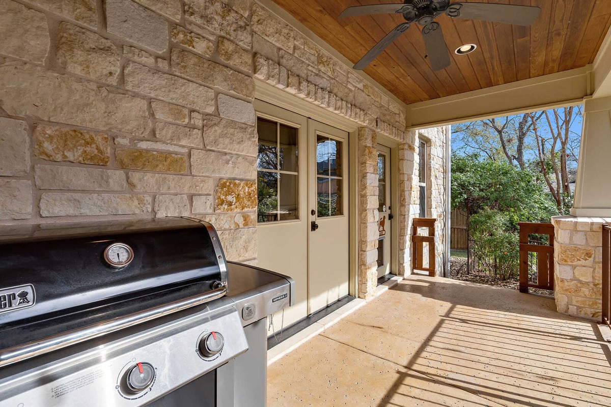 Outdoor stone patio with a grill and overhead ceiling fan in a custom Georgetown, TX home by J Bryant Boyd