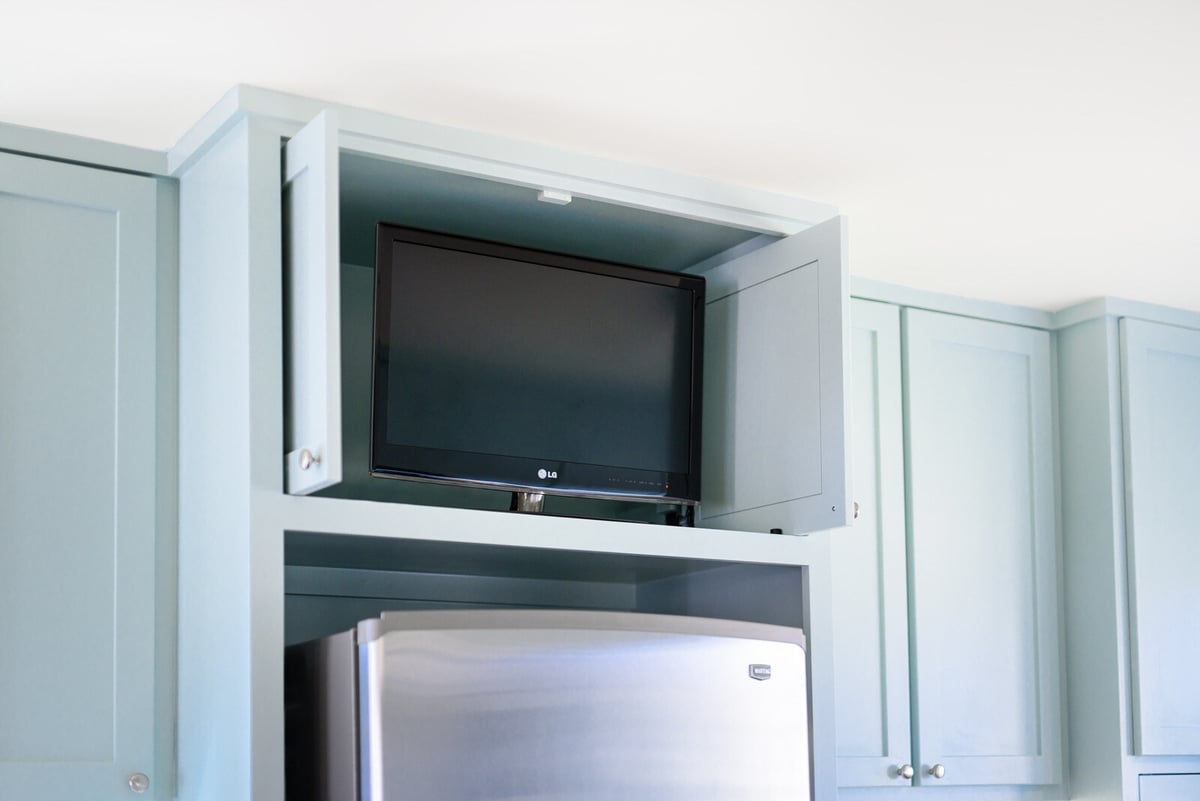 Hidden television in a light blue kitchen cabinet above a stainless steel fridge by J Bryant Boyd in Georgetown, TX