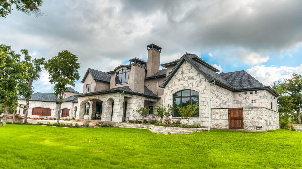 Grand exterior of a custom stone home with a well-maintained lawn by J Bryant Boyd in Georgetown, TX