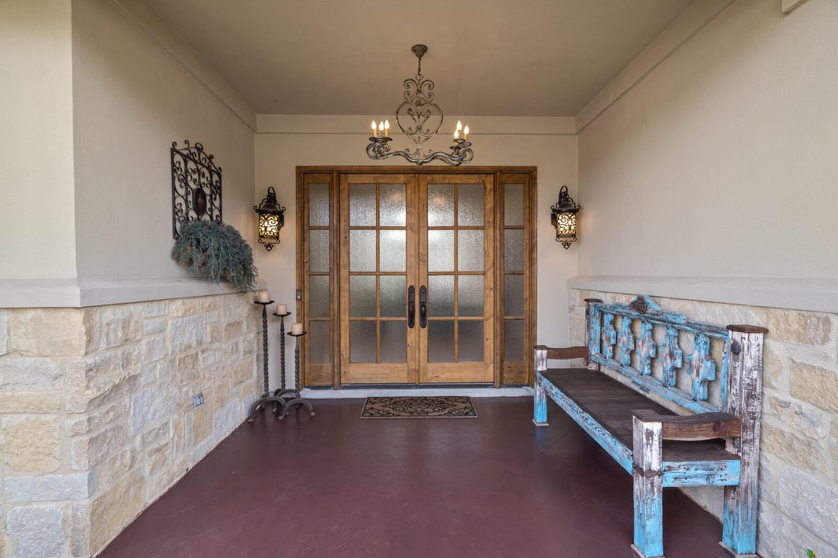 Covered porch of a custom home by J Bryant Boyd in Georgetown, TX, featuring a rustic wooden bench and decorative lanterns
