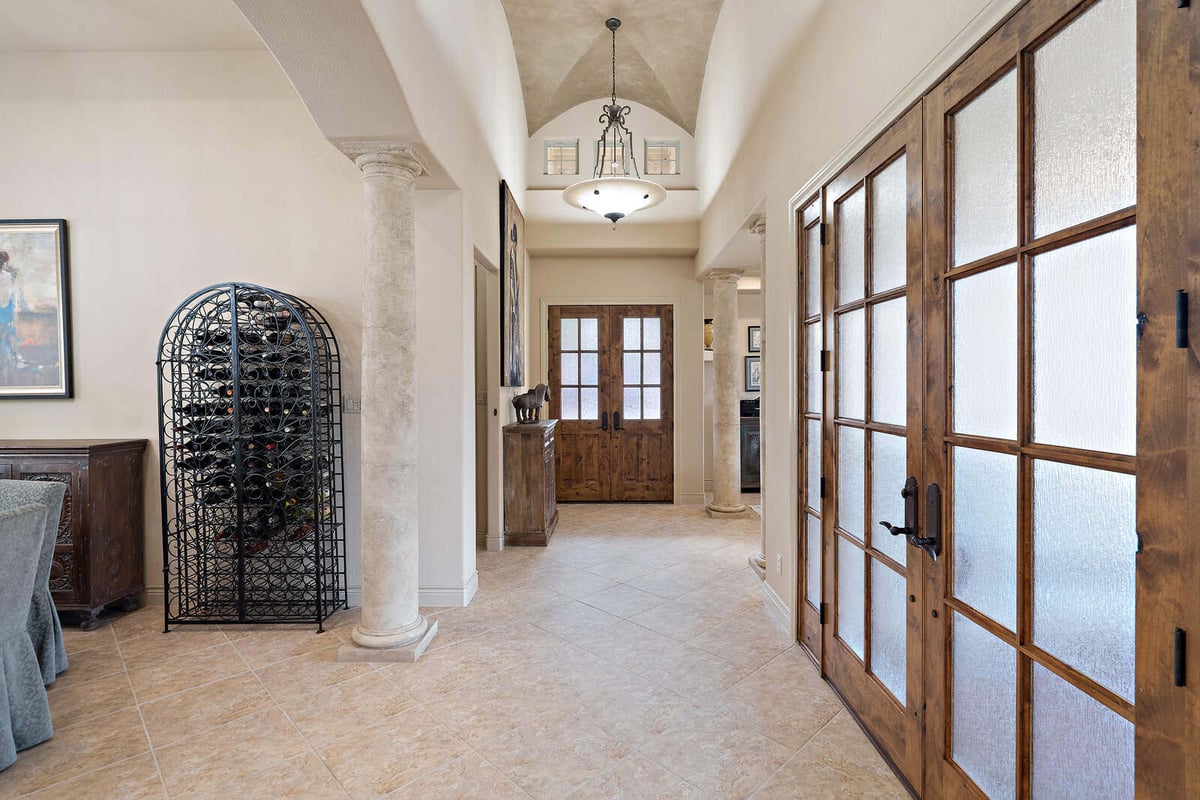 Elegant hallway with a wine rack in a custom home by J Bryant Boyd in Georgetown, TX, featuring stone columns and wooden doors