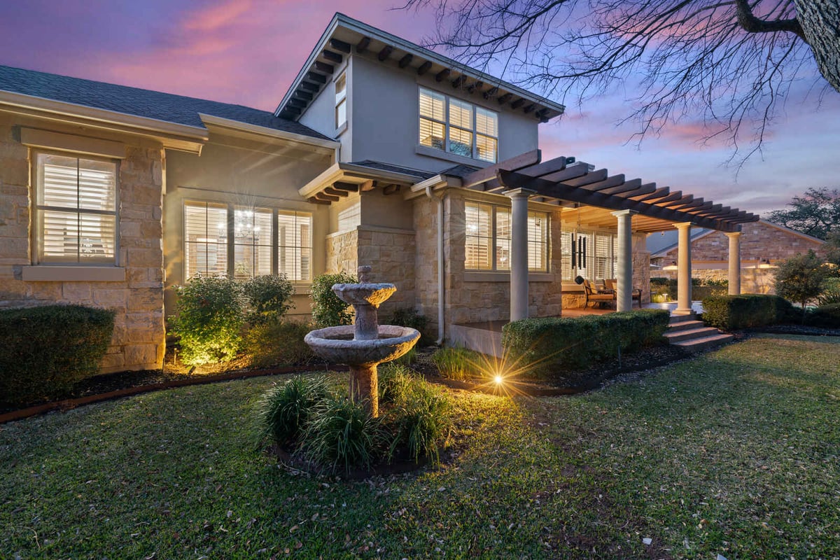 Well-lit backyard with a pergola and stone fountain at a custom home in Georgetown, TX by J Bryant Boyd