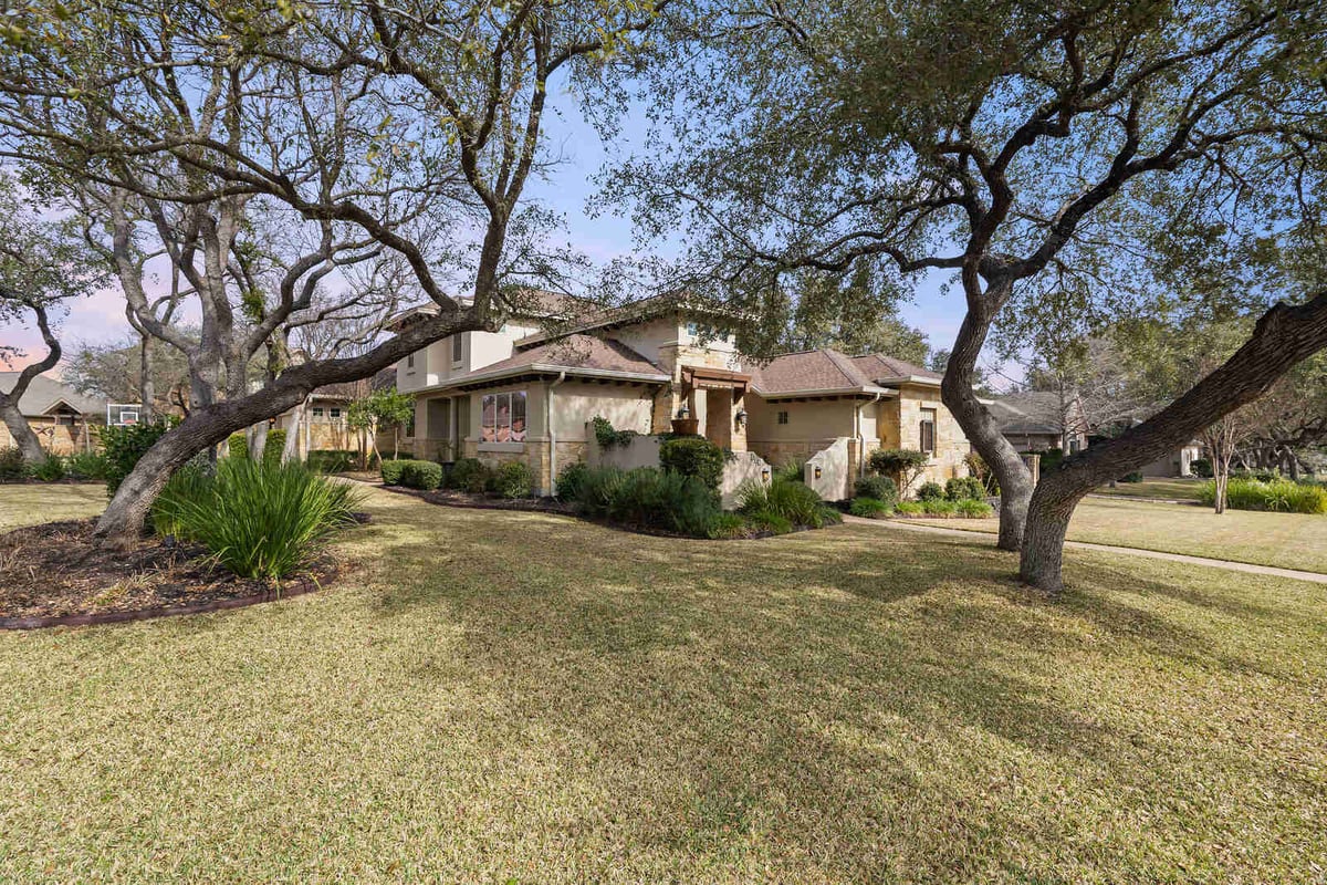 Well-maintained yard with mature trees surrounding a custom stone home in Georgetown, TX by J Bryant Boyd